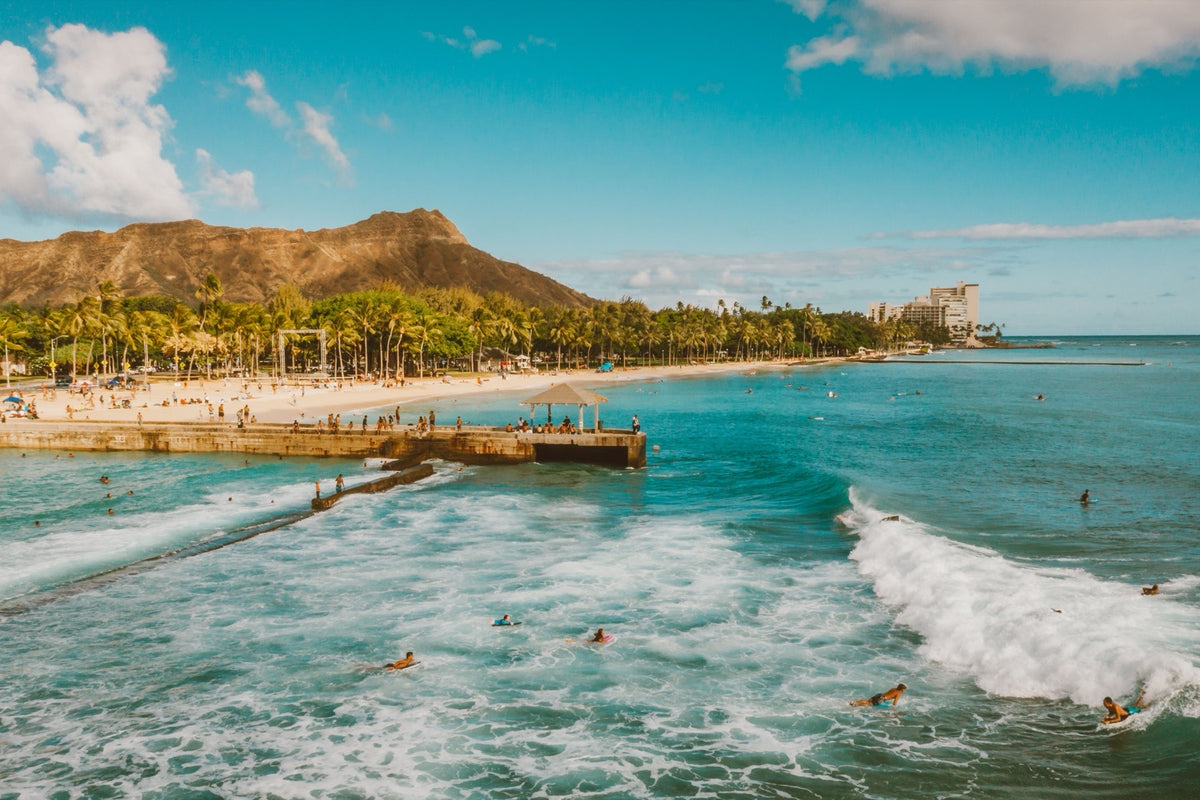 Surfers and swimmers off Waikīkī Beach with Diamond Head in the distance.