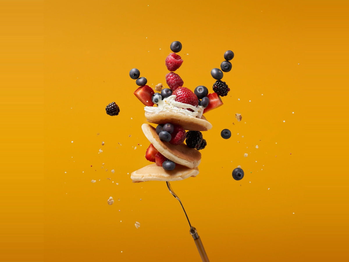 A stack of mochi pancakes on a fork with fresh berries mid-air against a mango background.